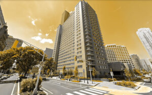 A large building stands over a crosswalk in an urban settings with a yellow tinted sky.