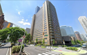 A tall building stands over a crosswalk, brightly lit by a sunny day and blue skies behind.